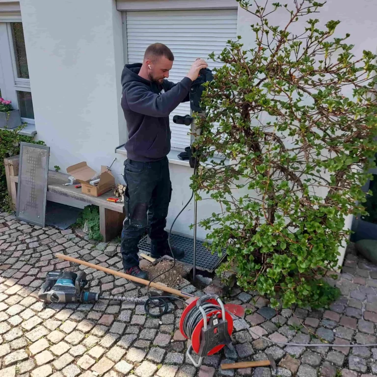Elektriker treibt mit einem Bodenbohrgerät einen Erdungsstab für eine Photovoltaikanlage in den Boden