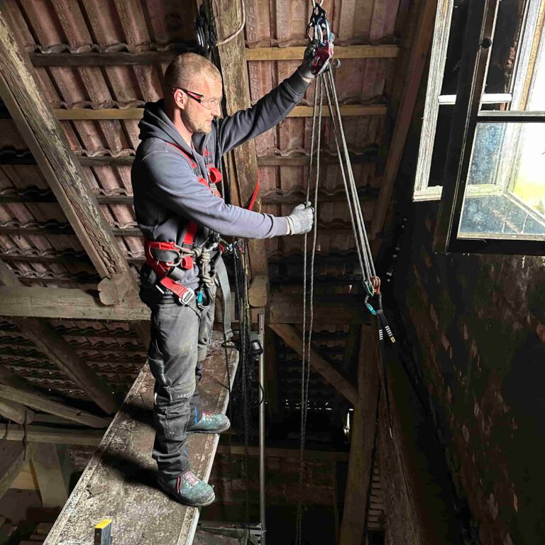 Industriekletterer mit Sicherheitsgeschirr senkt alte Solarmontagemodule im Dachbereich einer Photovoltaikanlage ab